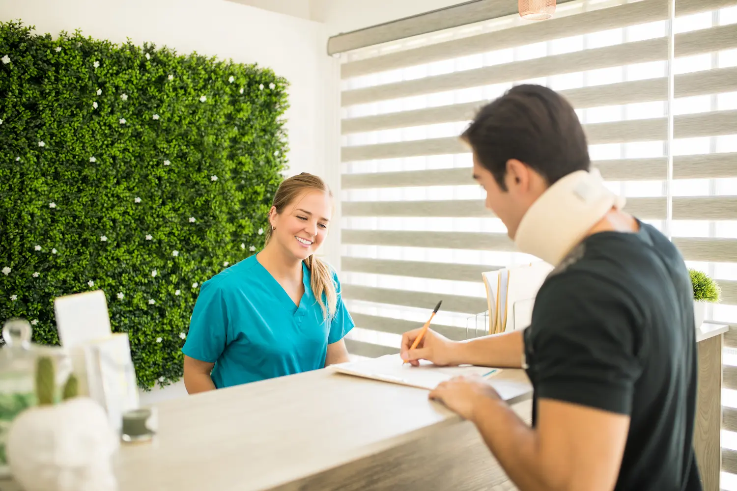 De la recepción de un hotel a la recepción de la clínica 4 una recepcionista de una clínica con uniforme azul atiende a un paciente con un collarín que firma un papel en la mesa alta