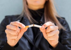 Relación entre la salud dental y la salud del corazón 6 en la foto se ve una mujer vestida de negro en primer plano, rompiendo un cigarro dado que quiere dejar de fumar porque el tabaquismo le ha llevado a contraer enfermedades cardiovasculares